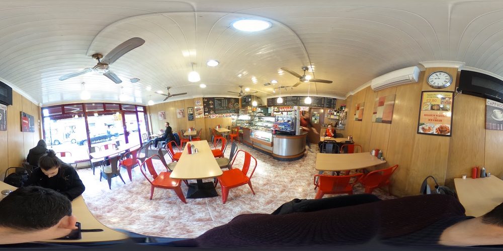 Wide view inside the cafe: red chairs, small tables, ceiling fans and the service counter