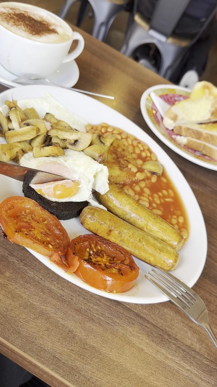 Cappuccino in a white cup beside grilled tomato, mushrooms and toast